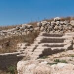panorama of a tourist in the entrance courtyard of tel lachish ruins in Israel showing the city wall, inner gate, and official rooms