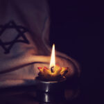 The star of David and candle stands on the table on a black background in memory of the victims of the Holocaust and genocide.