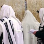 Orthodox Jews wearing tallit shawls are praying with Siddur prayer books at the Western/Wailing Wall or Kotel, holiest site in Judaism; Jerusalem Israel