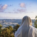 Succot (Feast of Tabernacles) in Jerusalem: Jewish man in a Tallit praying while waving the Four Species, with a view towards the Temple Mount, the Old City and the Mount of Olives