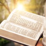 Person reading book praying with Bible