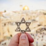 JERUSALEM, ISRAEL. February 15, 2019. Hand holding a Star of David, a Jewish religious symbol against the Western wall of the Jewish Temple in the Old city of Jerusalem. Judaism Zionism concept image.