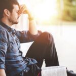 A young male sitting on the ground and holding the bible in his hands-thoughtful, mindful concepts